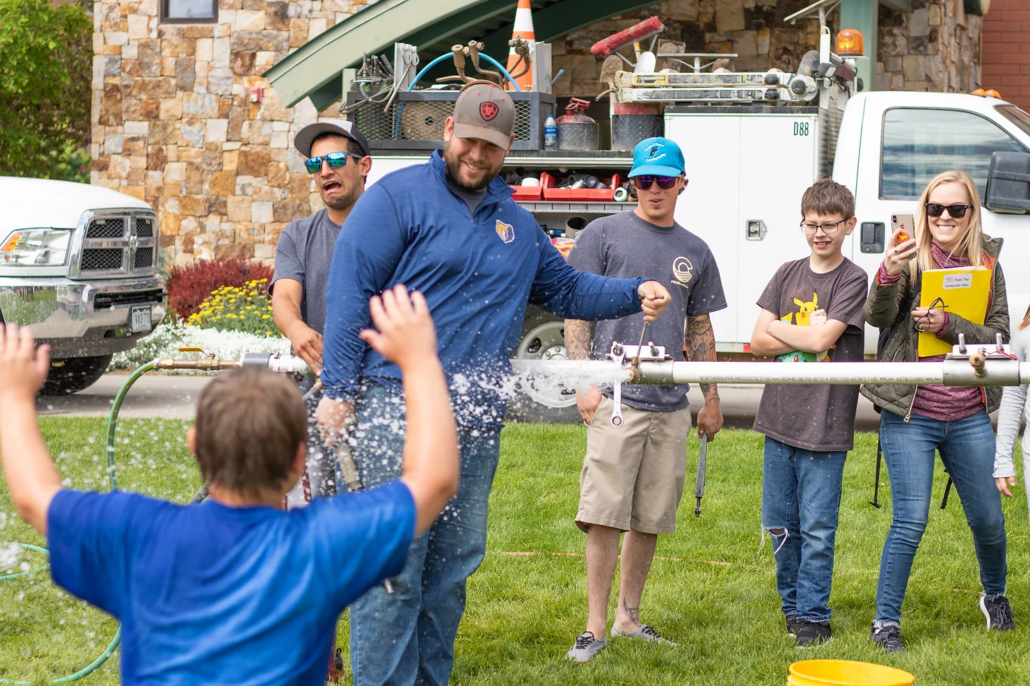 Children and adults enjoying a water rocket experiment outdoors, with laughter and excitement.
