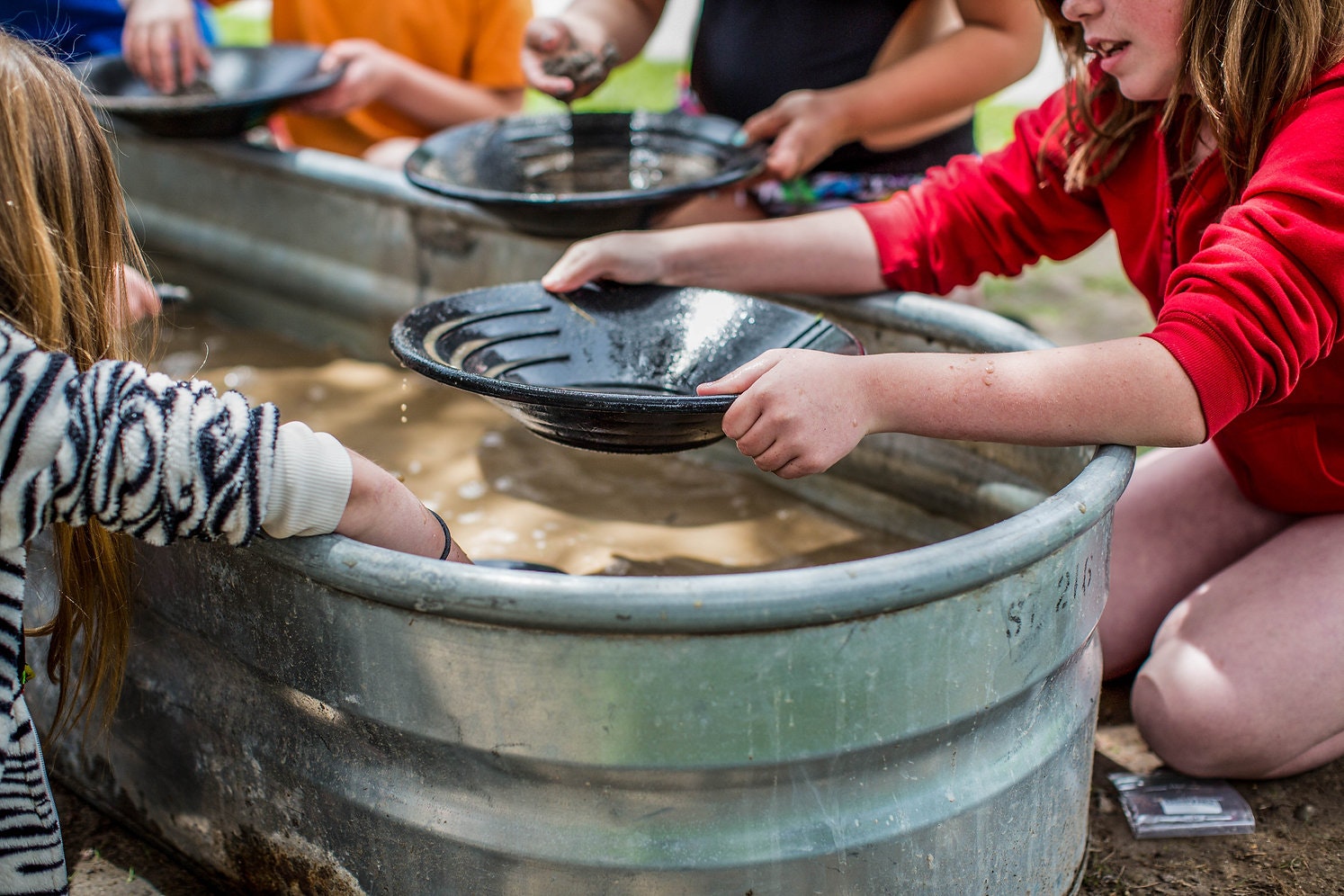 Children are panning for gold using pans and a water-filled trough.