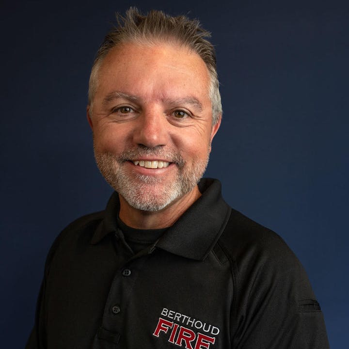 A smiling person wearing a shirt with a fire department logo.