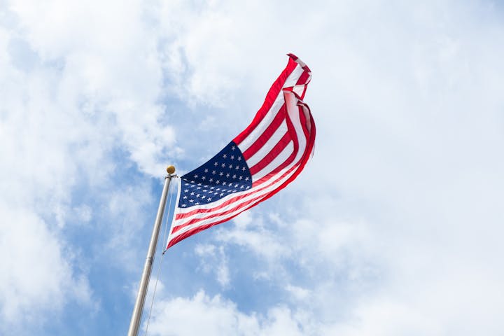 A U.S. flag waving against a cloudy sky.
