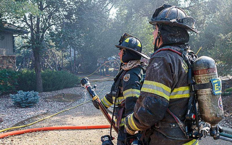 Two firefighters with hoses, ready for action amidst smoky surroundings.