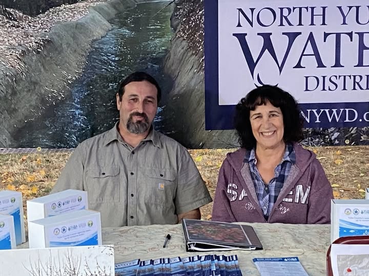 Two people sitting at a booth for North Yuba Water District, with brochures and a banner.
