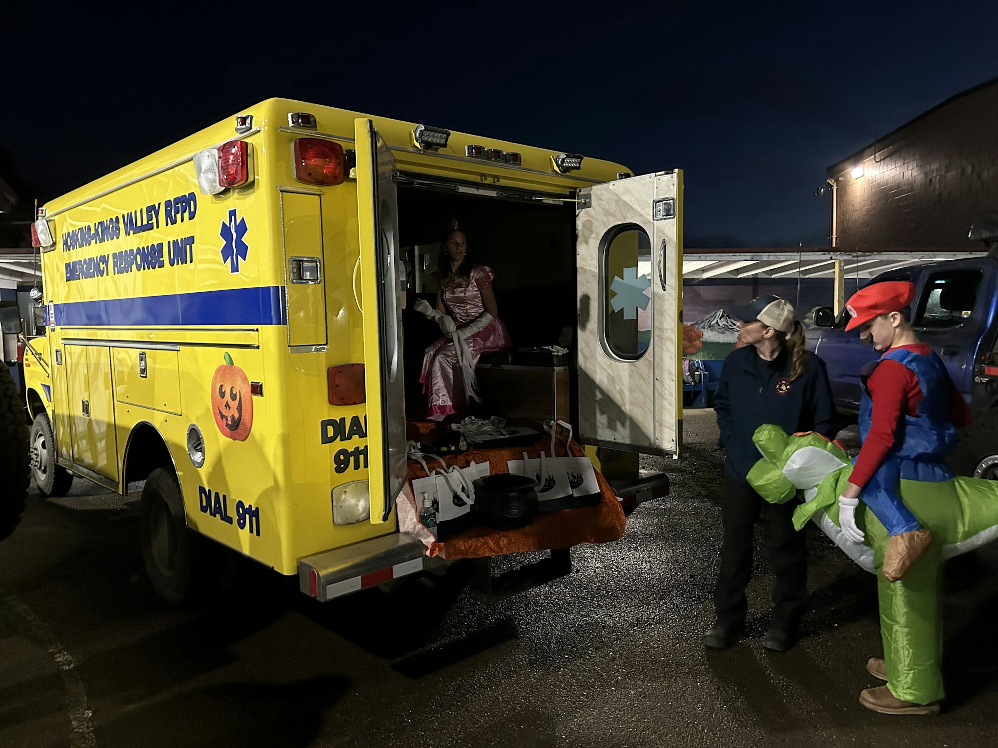 An emergency response unit is parked, with people in costumes; one dressed as Mario and another as a princess.