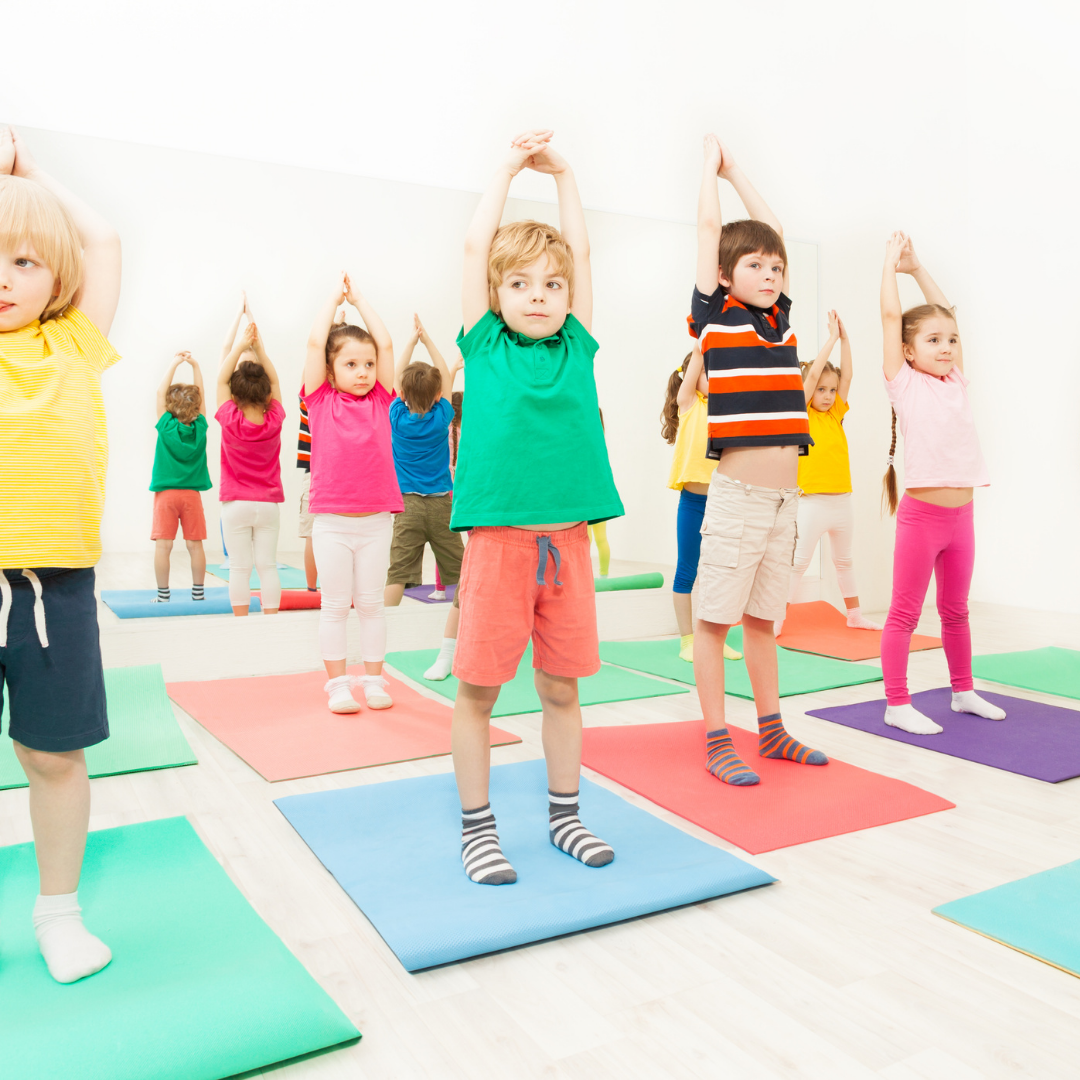 A group of children in colorful outfits practice yoga poses on mats in a bright, spacious room.