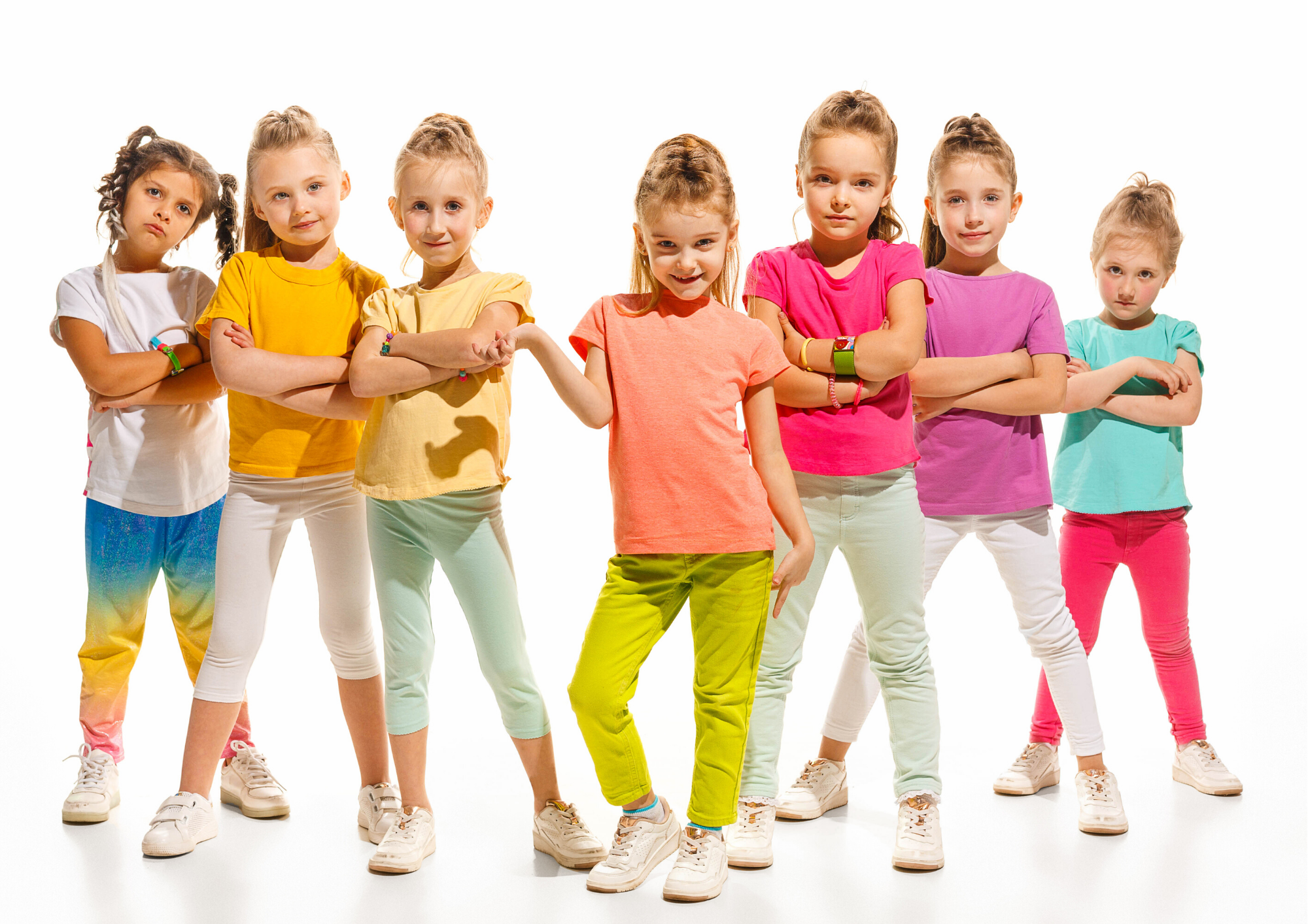 A group of seven girls poses confidently, dressed in colorful shirts and pants, against a white background.