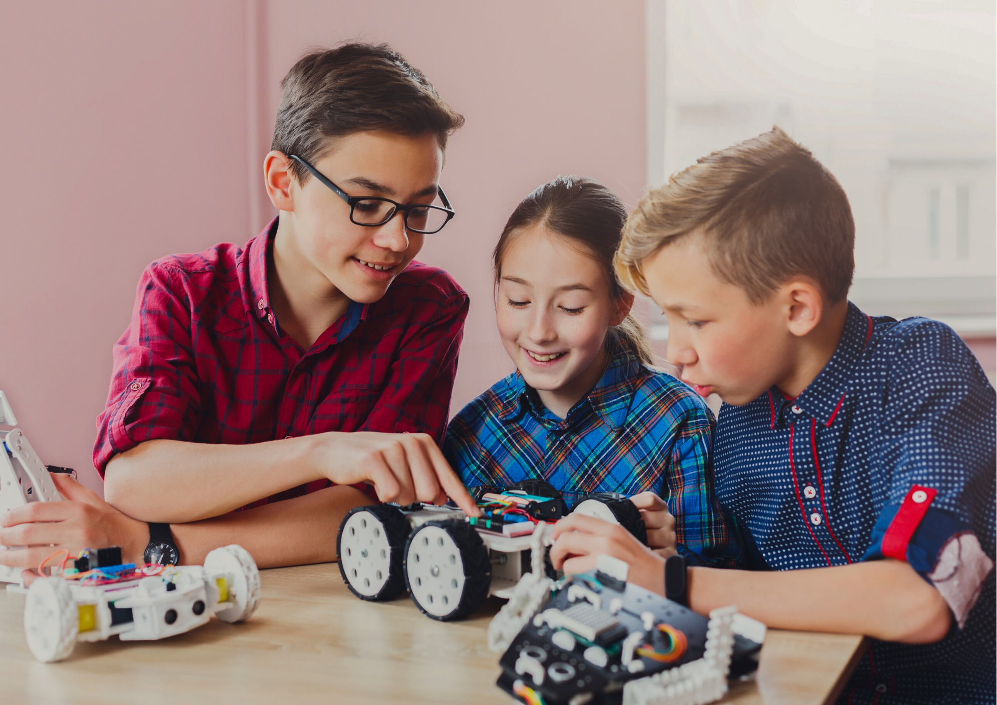 Three kids are collaborating on building or programming robots at a table, immersed in their project with enthusiasm.