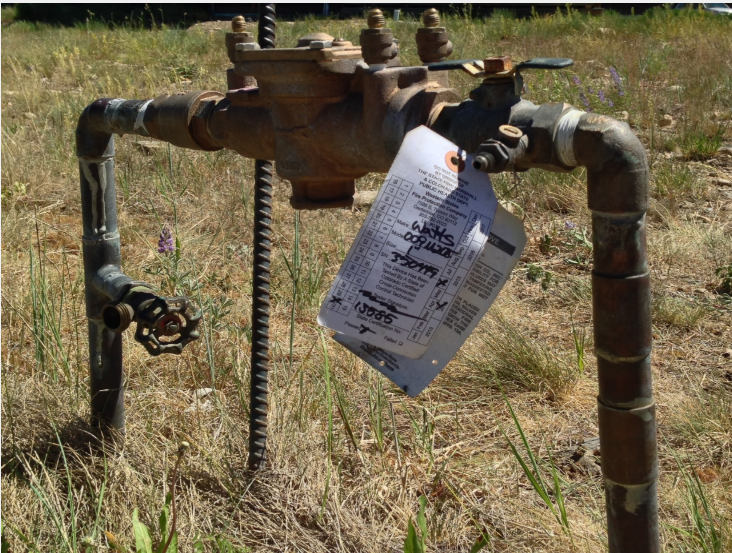 Rustic outdoor water pipes and valves with a tagged notice attached.