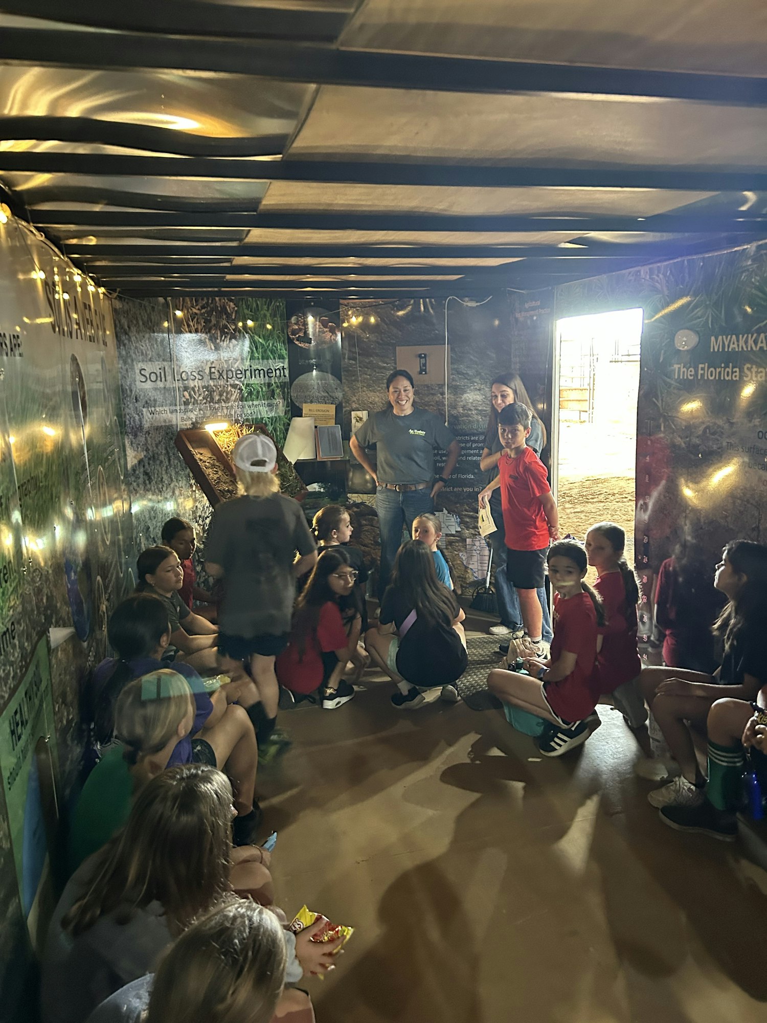 A group of students sitting in an interactive space, engaging with displays about soil and environmental education.