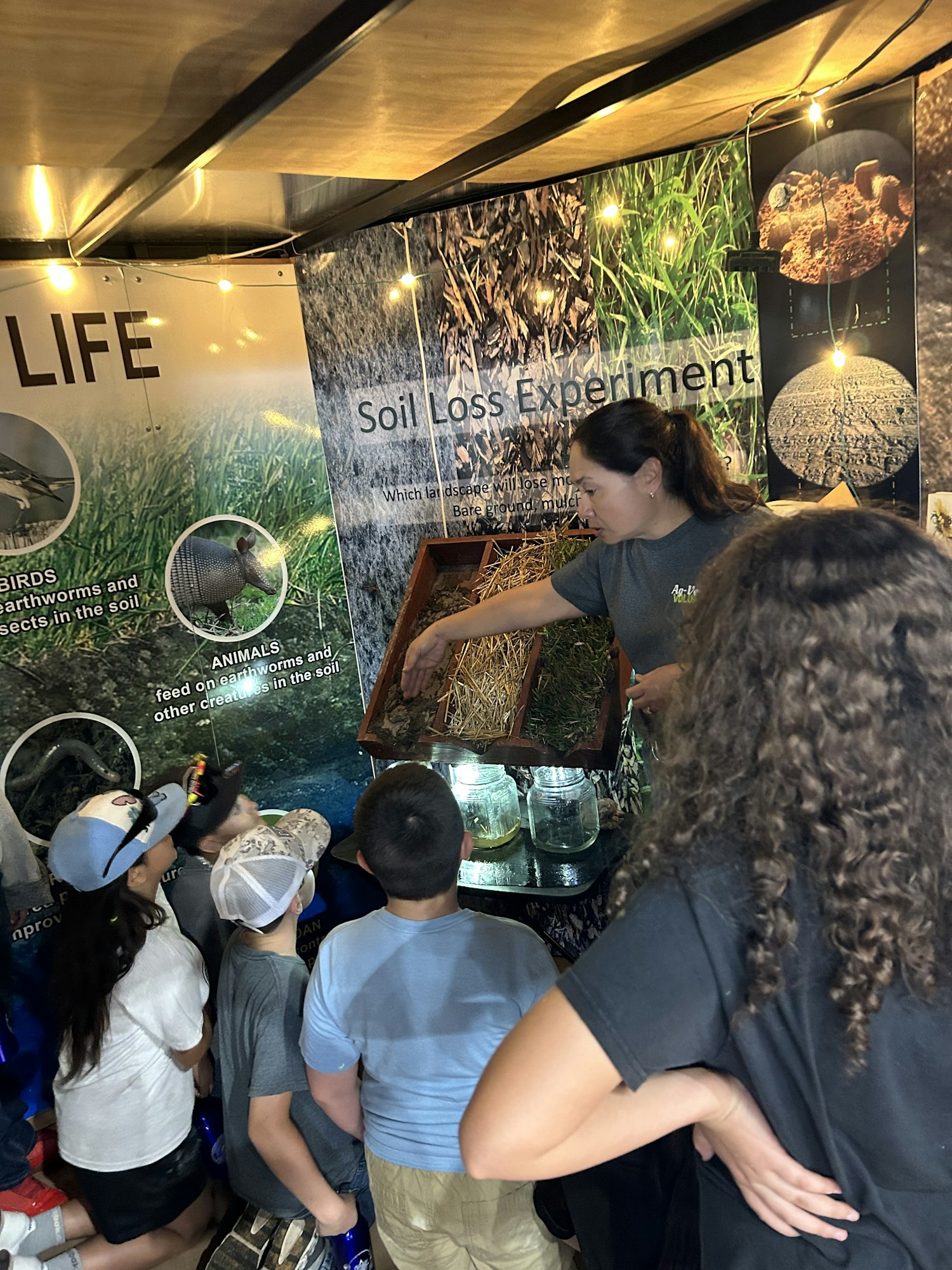 A presentation on soil loss with a demonstrator engaging children, featuring displays about soil and its importance.