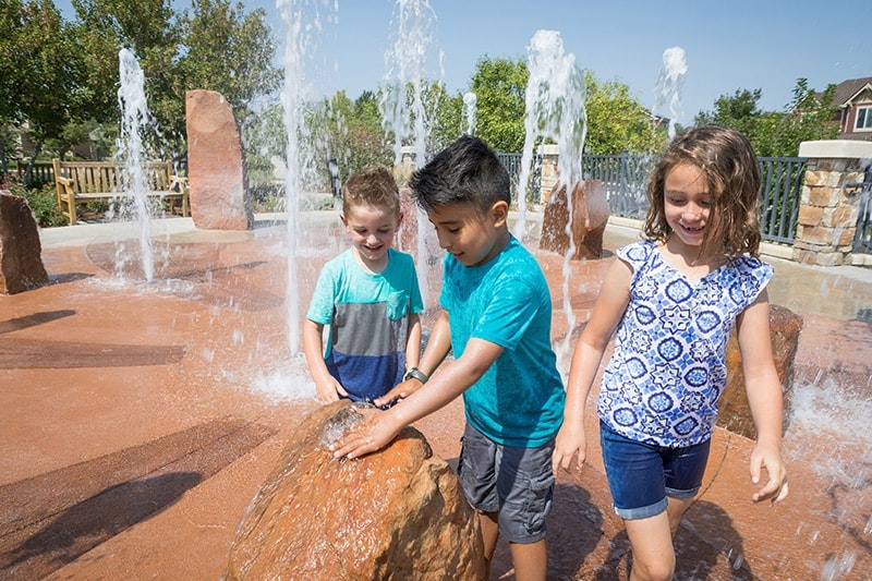 Children playing at a water fountain on a sunny day.