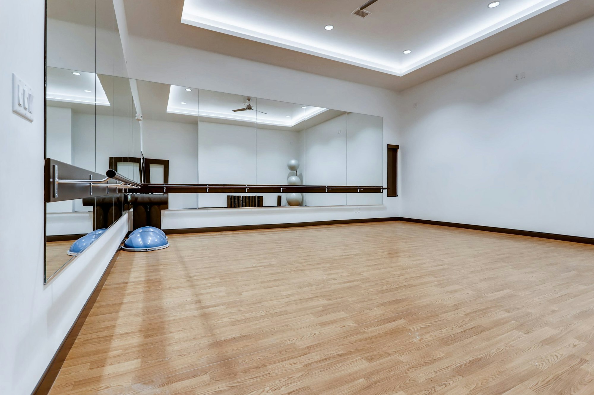 A spacious room with wooden flooring, mirrors, ballet barres, and exercise balls.