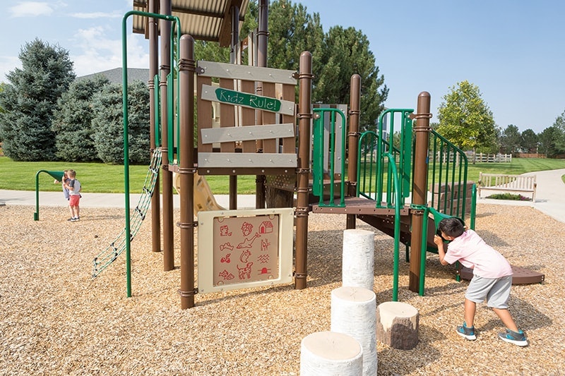 Children playing on a playground with slides, climbing nets, and educational panels.