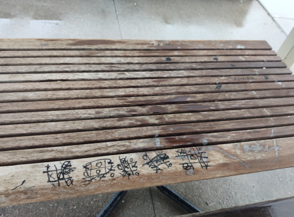 A wet wooden bench with tic-tac-toe games doodled on it.