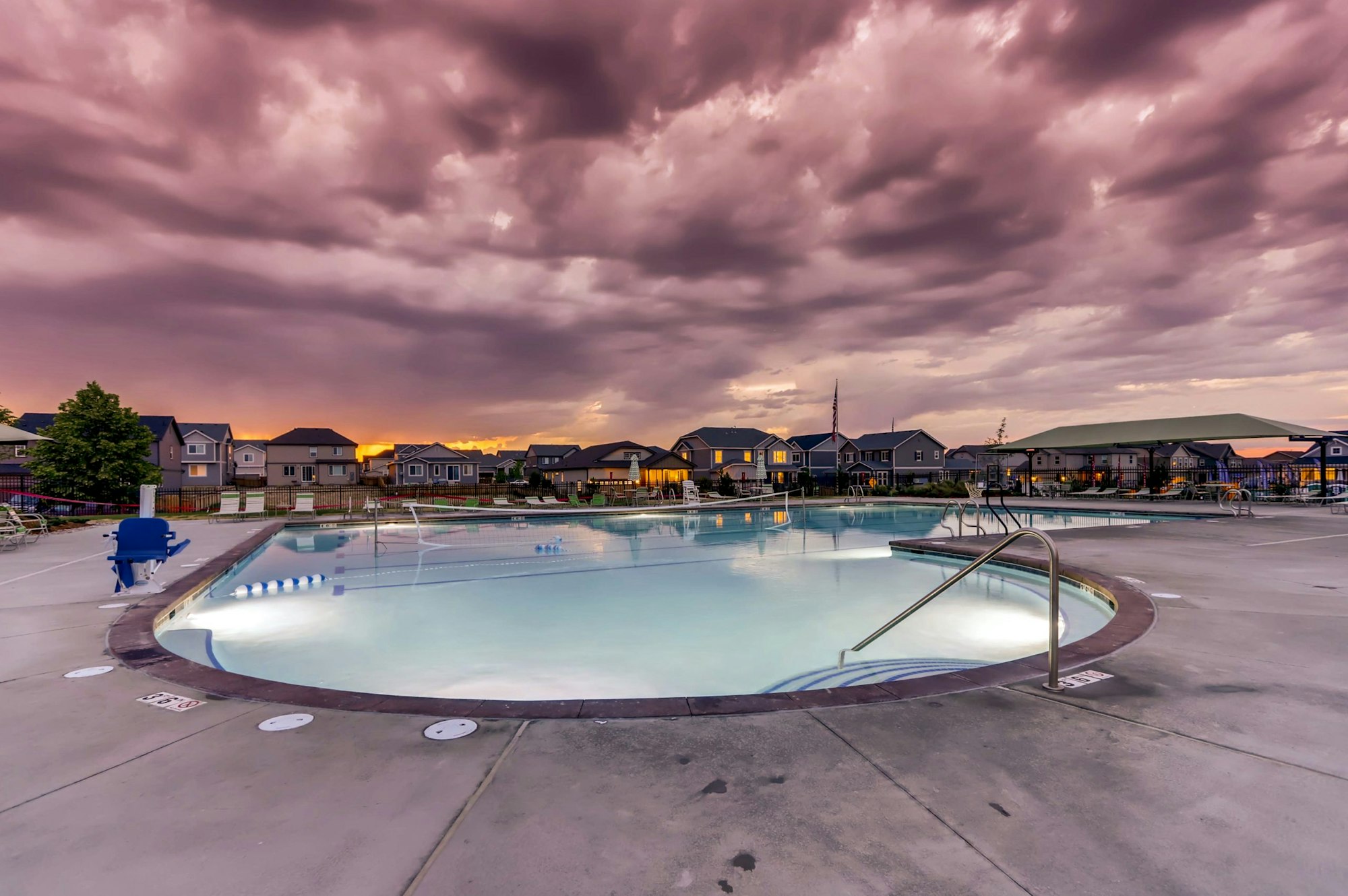 A community pool with dramatic purple clouds at sunset, surrounded by houses.