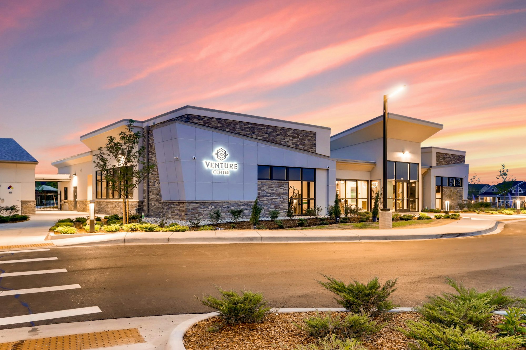 Modern commercial building, "Venture Center" sign, sunset sky, parking lot, landscaped area.
