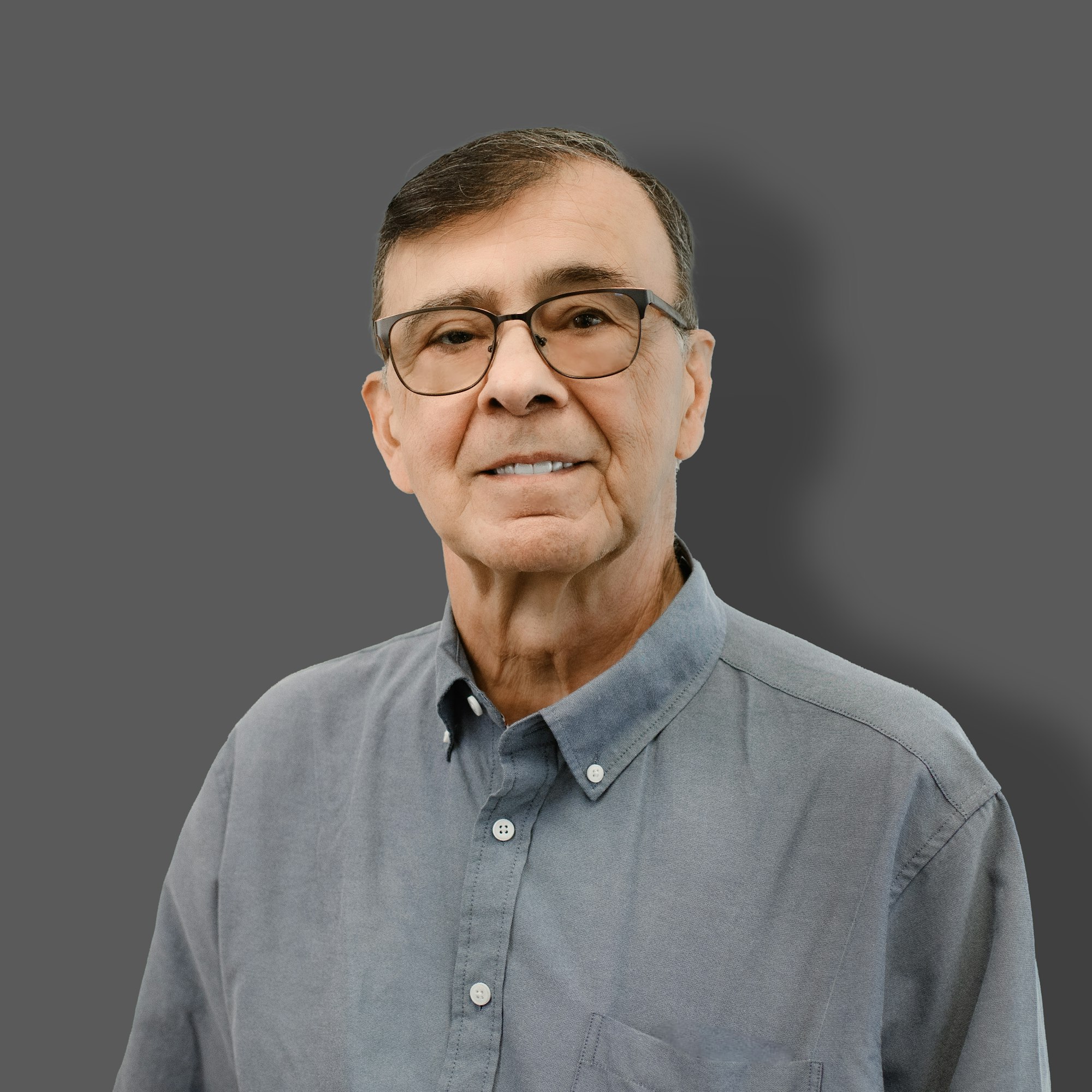 The image features an older man smiling, wearing glasses and a buttoned shirt, set against a grey background.