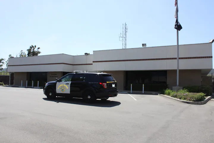 A police SUV parked in front of a building with palm trees and a clear sky.