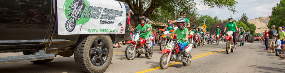 A parade with young motorcycle riders in green shirts, accompanied by a truck with "Rocky Mountain Sport Riders" banner.