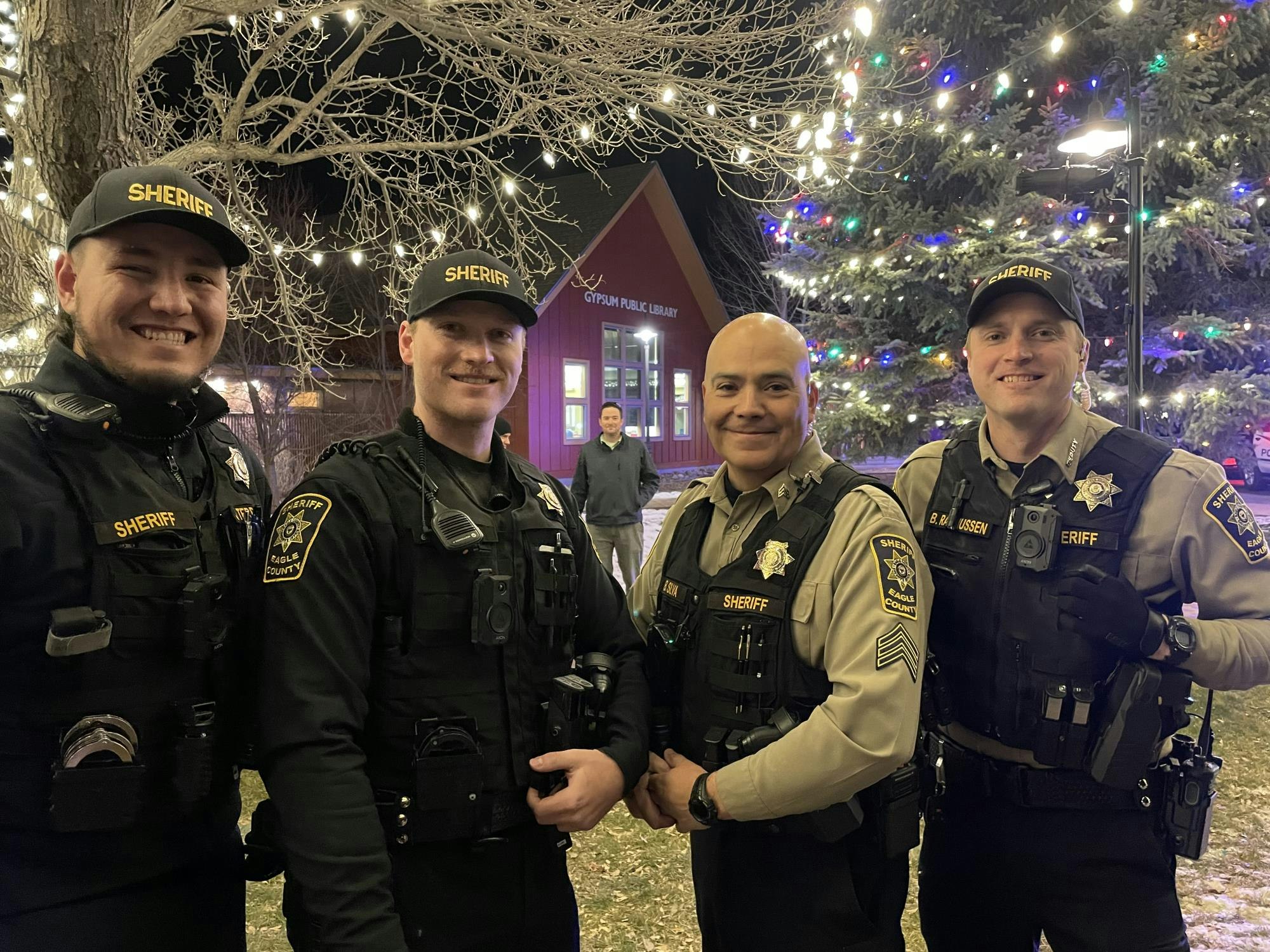 Four sheriffs smiling in front of a lit tree and building.