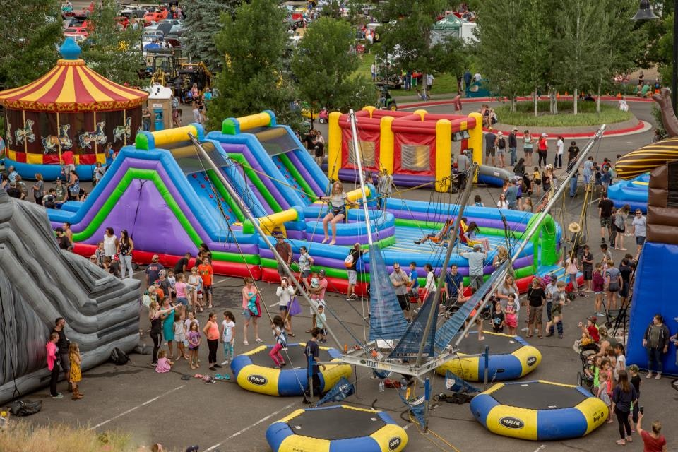 A fun fair with inflatable slides, bounce houses, a carousel, and trampolines, crowded with people enjoying the activities.