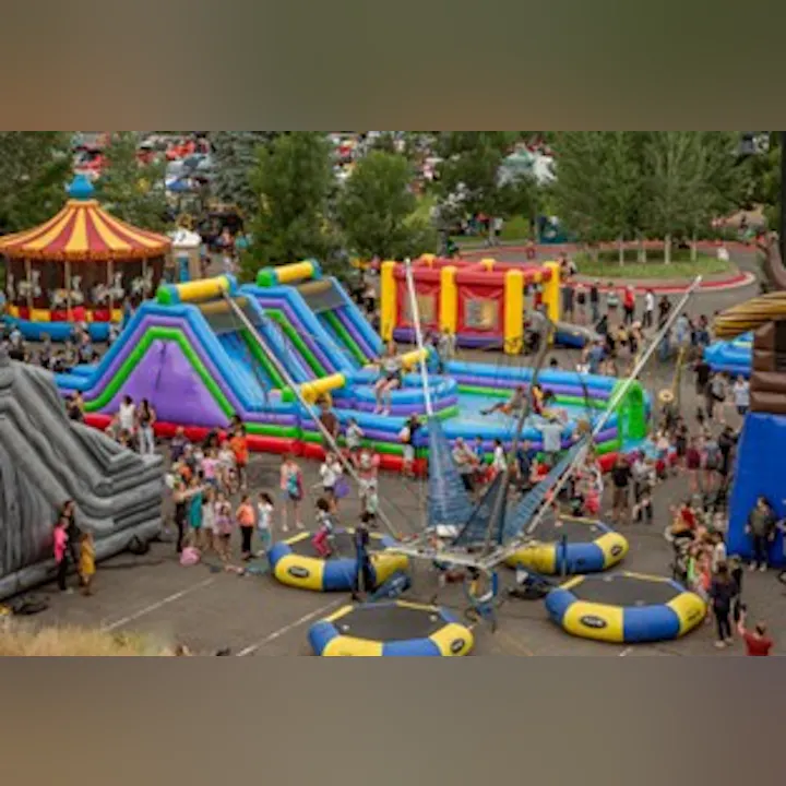 A vibrant outdoor fair with colorful inflatable bounce houses, a water slide, and many people enjoying various activities.