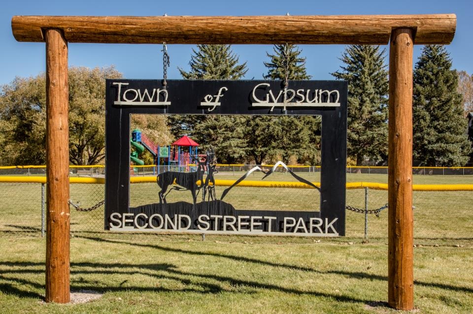 Sign for "Town of Gypsum, Second Street Park" with playground and trees in the background.