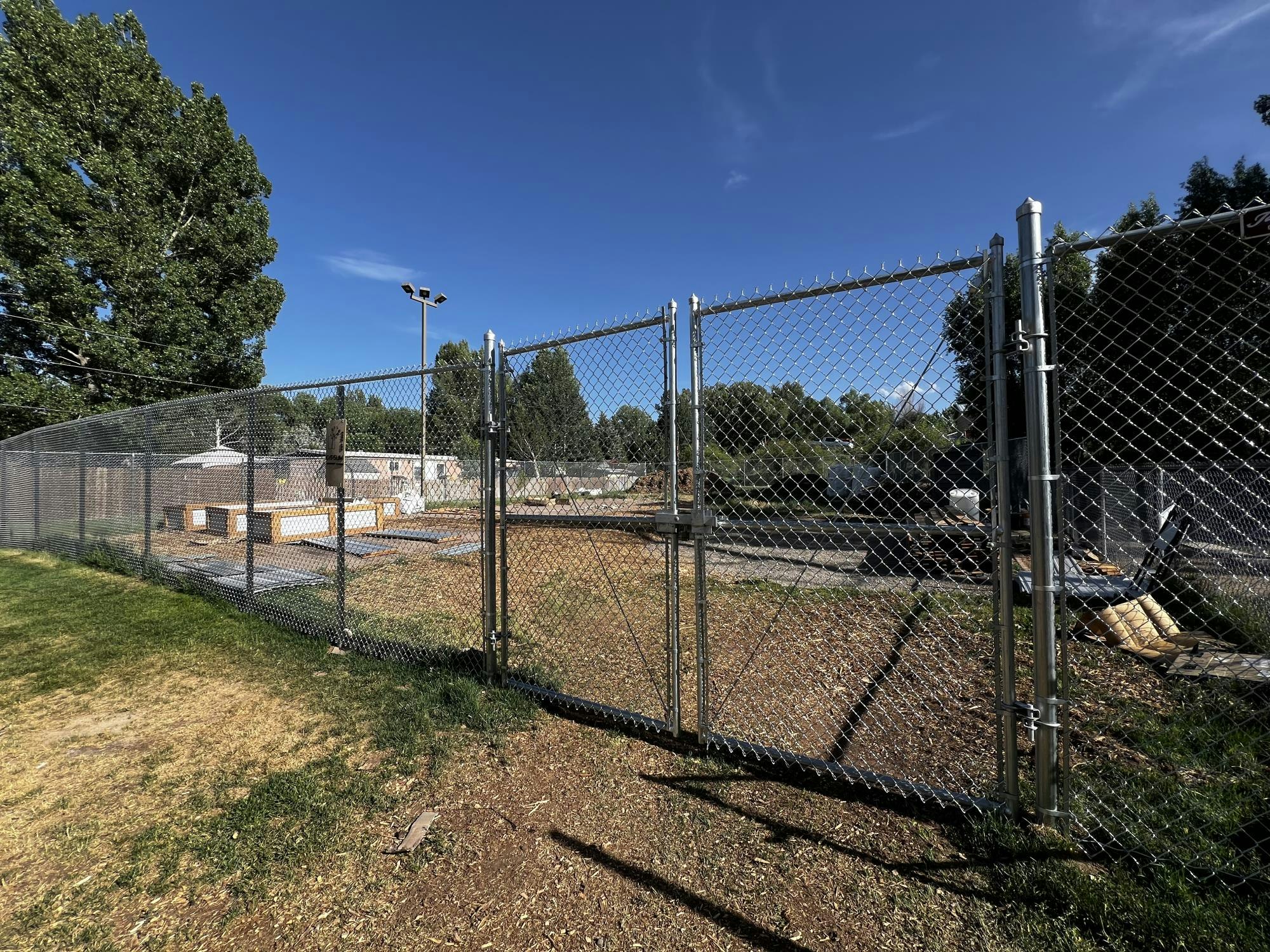 A chain-link fence surrounds a park area under a clear blue sky, with trees in the background.