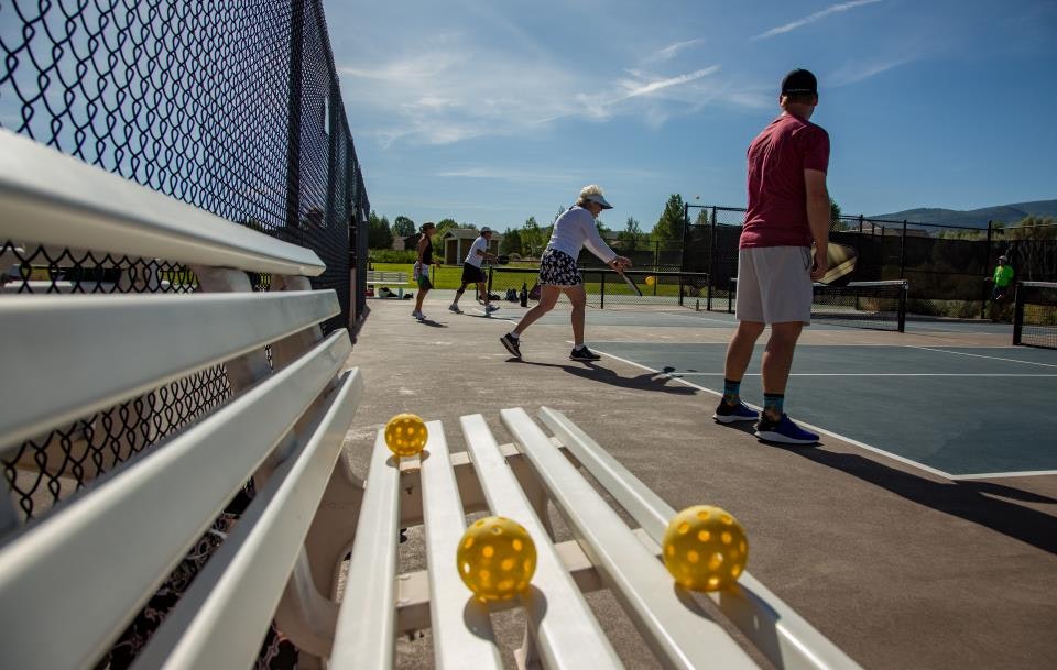 People playing pickleball on outdoor courts with a bench and pickleballs in the foreground.