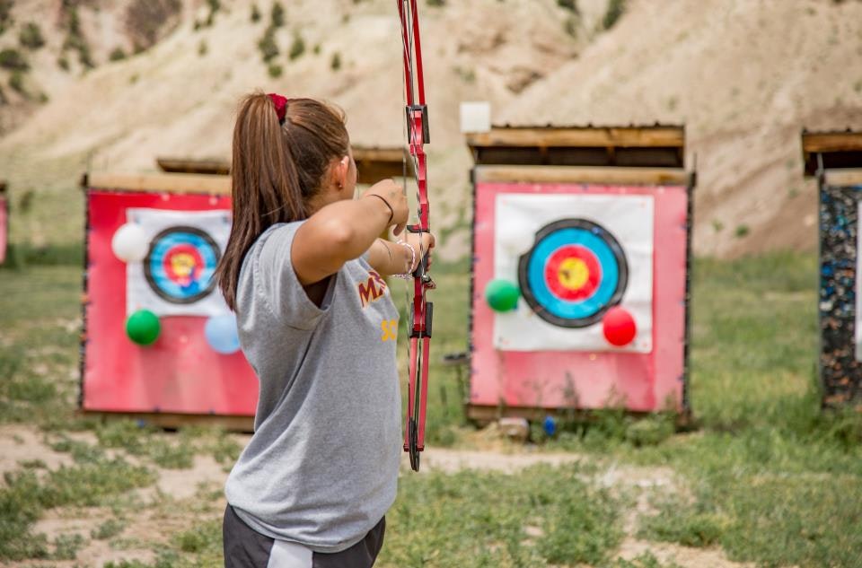Person aiming a bow at archery targets outdoors, with colorful balloons attached.