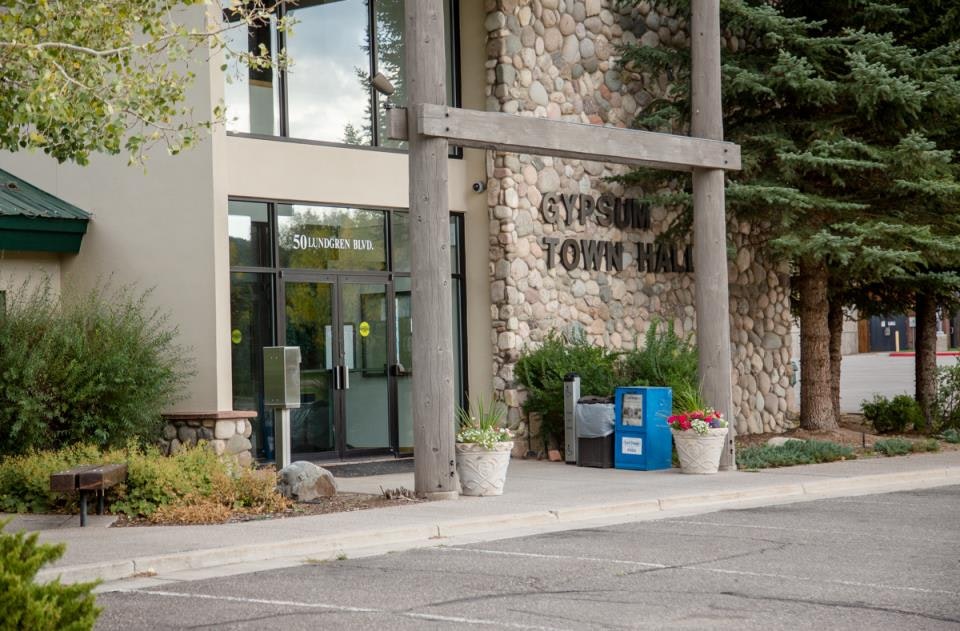 Entrance to Gypsum Town Hall, with stone facade, glass doors, potted plants, and trees.