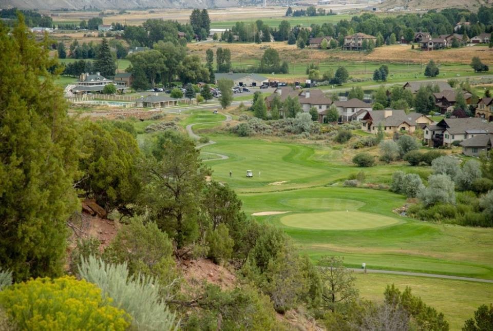 A scenic view of a lush golf course surrounded by trees and houses, with hills in the background.
