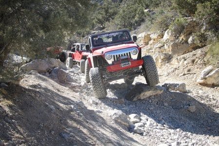 Red off-road vehicles navigating a rocky trail in a forested area.