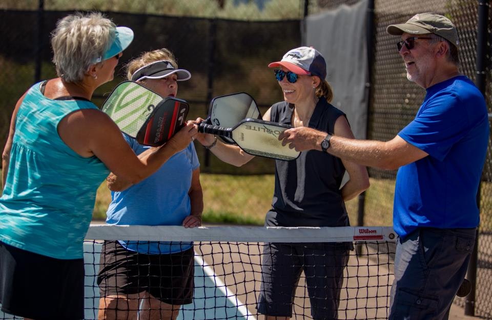 Four people on a pickleball court, holding paddles together in the middle.