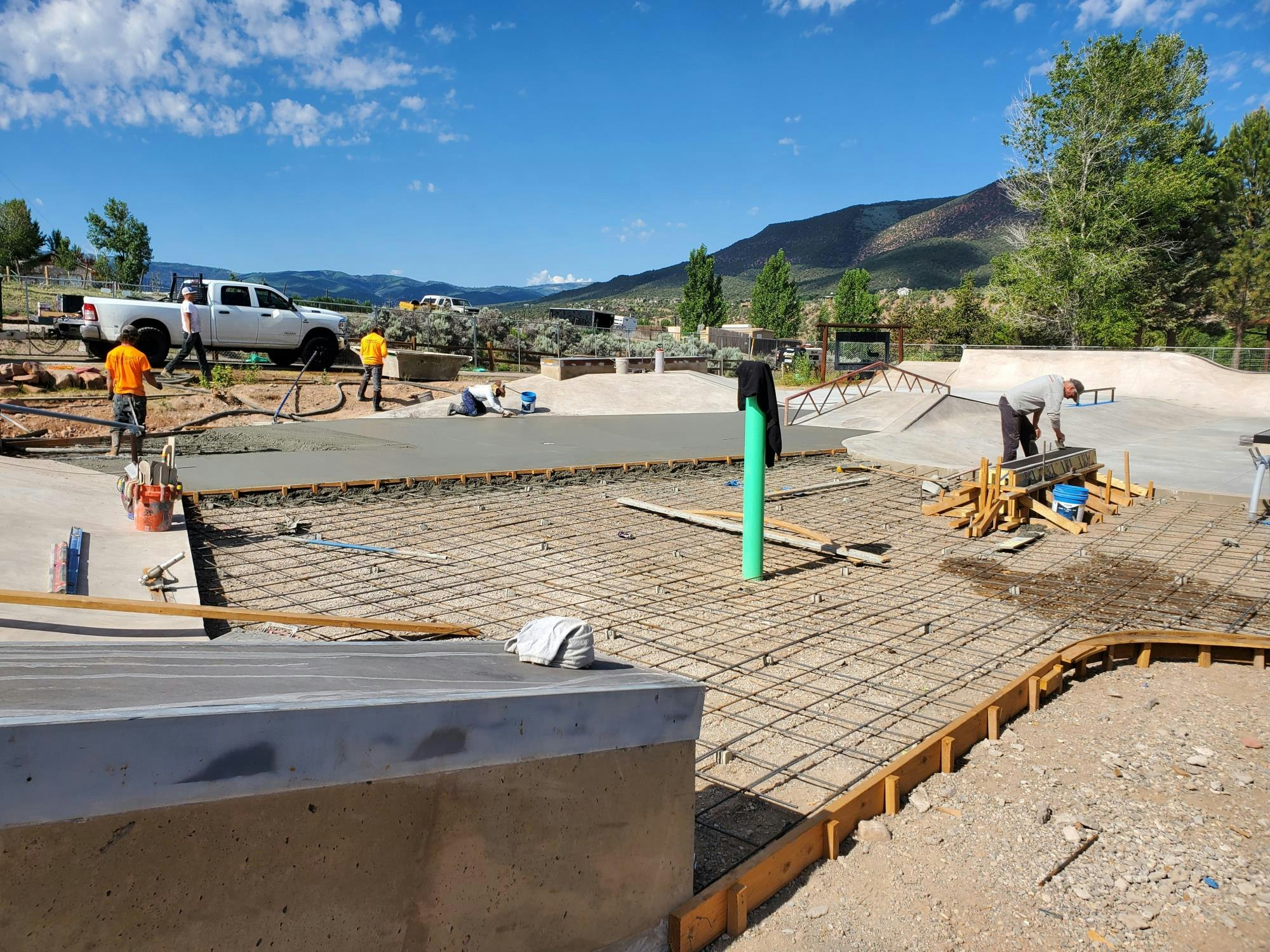 Workers and truck at a skatepark construction site, with rebar and concrete.