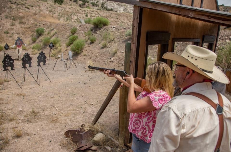 Two people at a shooting range; one is aiming a rifle at various metal targets.