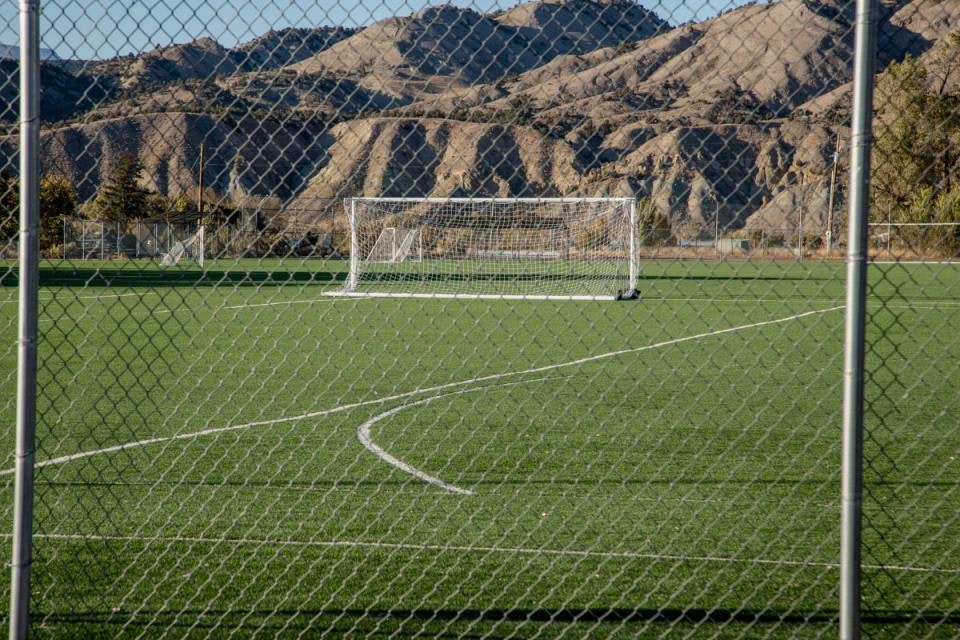 A soccer field with a goal, surrounded by a chain-link fence, and mountains in the background.