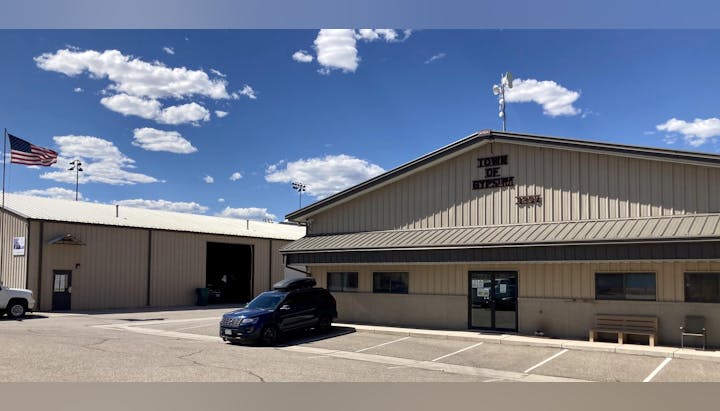 Metal building with "Town of Gypsum" sign, American flag, cars, clear sky.