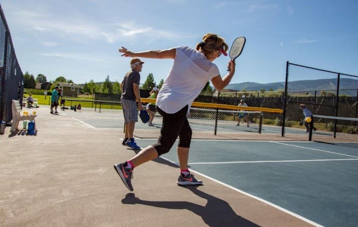People playing pickleball on outdoor courts under a clear blue sky.