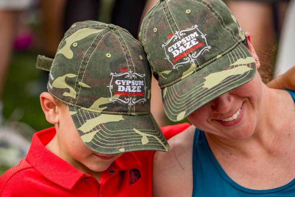 Two people wearing matching camouflage caps with "Gypsum Daze" logo, smiling closely together.