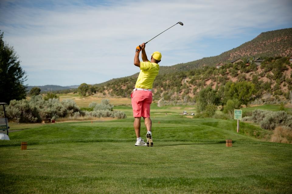 Golfer in bright attire completing a swing on a lush golf course with mountainous background.