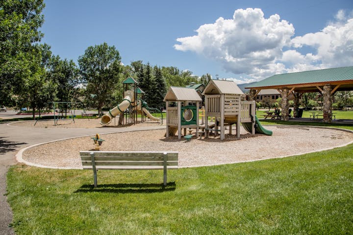 A playground with slides, play structures, swings, a bench, and a pavilion on a sunny day.