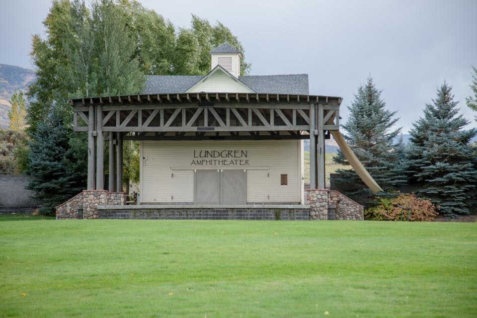 Outdoor amphitheater stage with "Lundgren Amphitheater" sign, surrounded by trees and grass.
