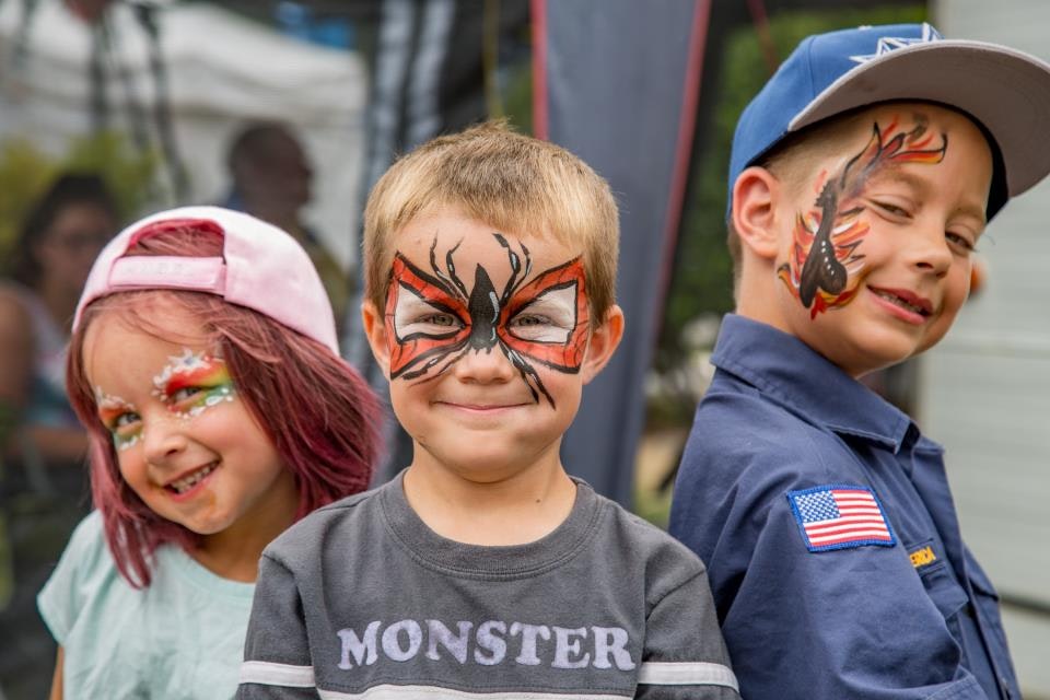 Three kids with colorful face paint, smiling and posing.