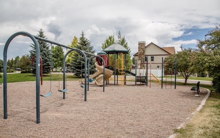 A playground with swings, slides, climbing structures, and a nearby house, surrounded by trees.