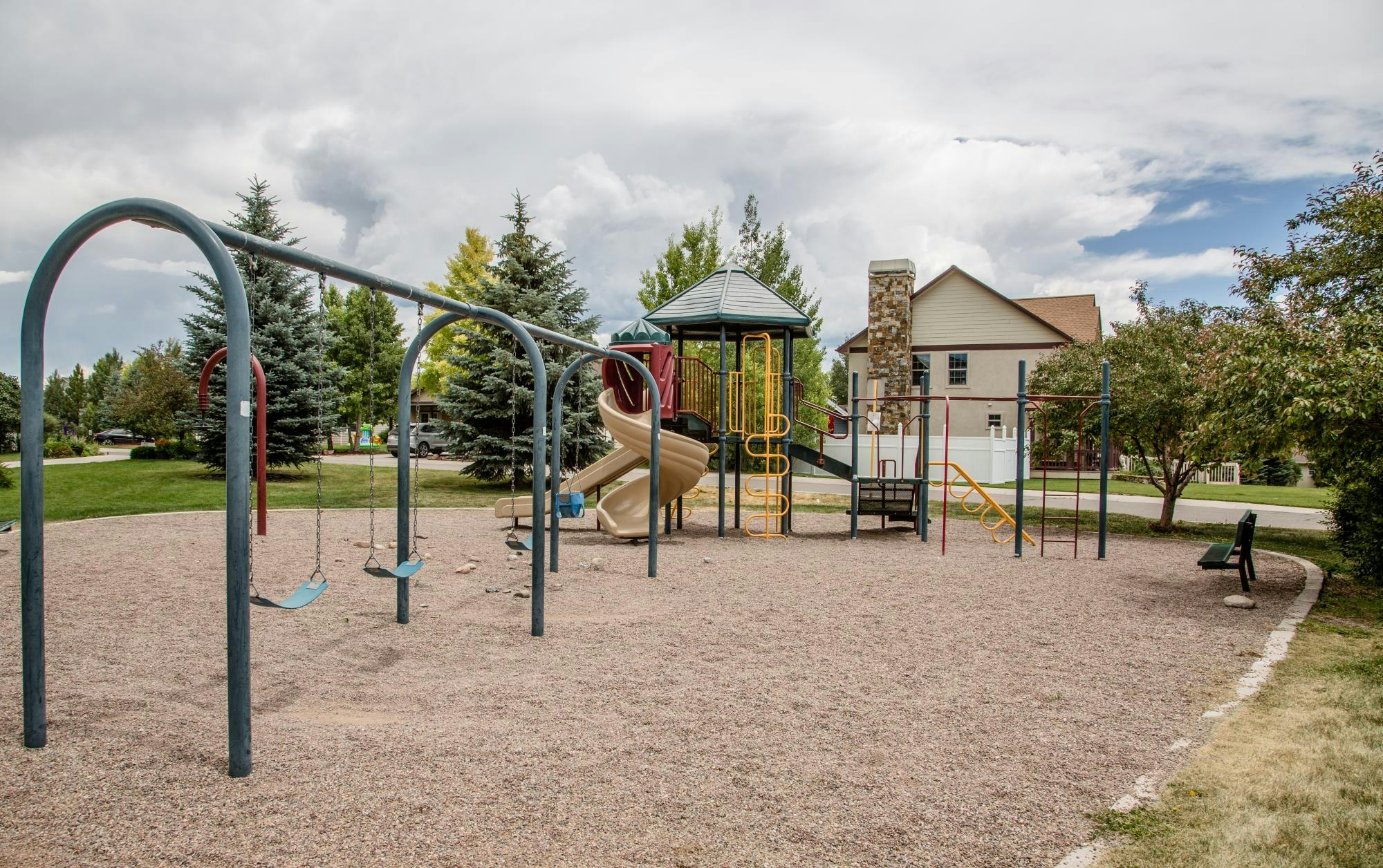 A playground with swings, slides, climbing structures, and a nearby house, surrounded by trees.