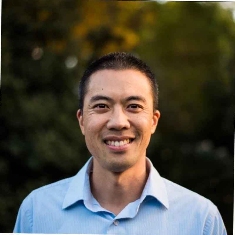 A person in a blue shirt smiling in front of a blurred green background.