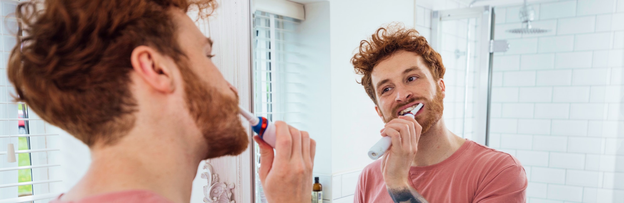 A man brushes his teeth, looking at the mirror in a bright bathroom.