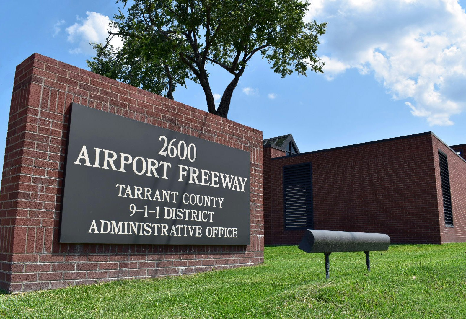 A sign for "2600 Airport Freeway, Tarrant County 9-1-1 District Administrative Office" in front of a brick building.