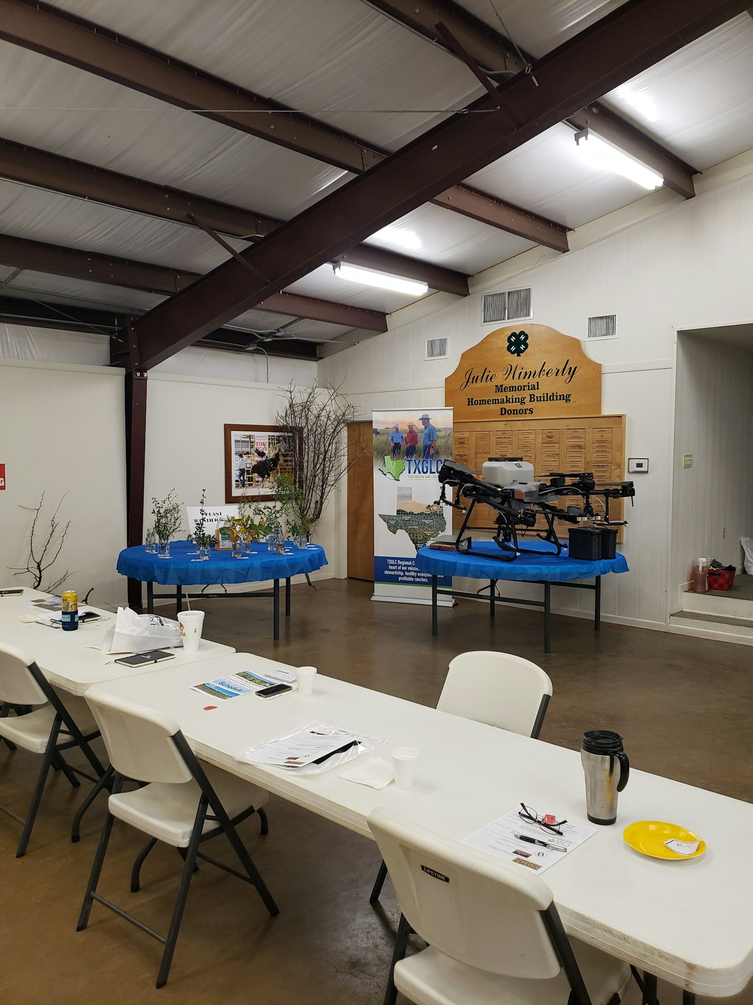 Room with a table setup, displays showing plants and a drone, educational materials on tables, and a sign for a memorial homemaking building.