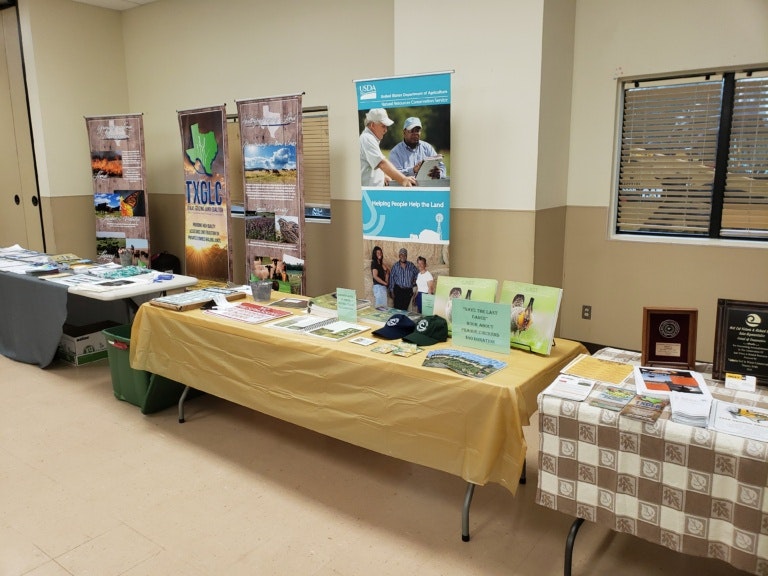 Table display with brochures, hats, and posters about land conservation and agriculture.
